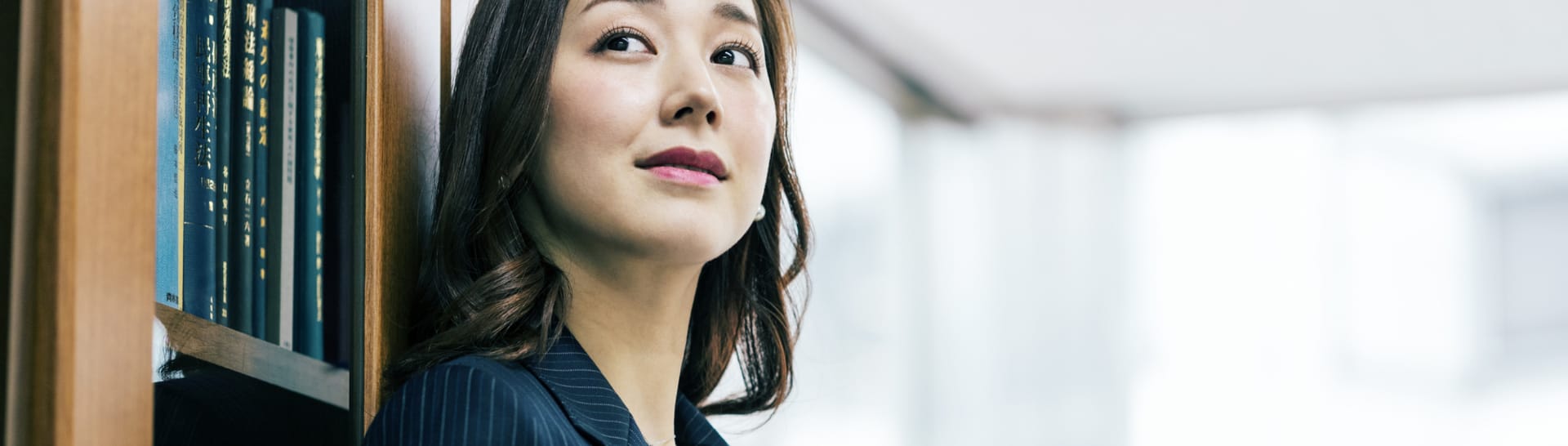 本棚によりかかるビジネスウーマンの写真