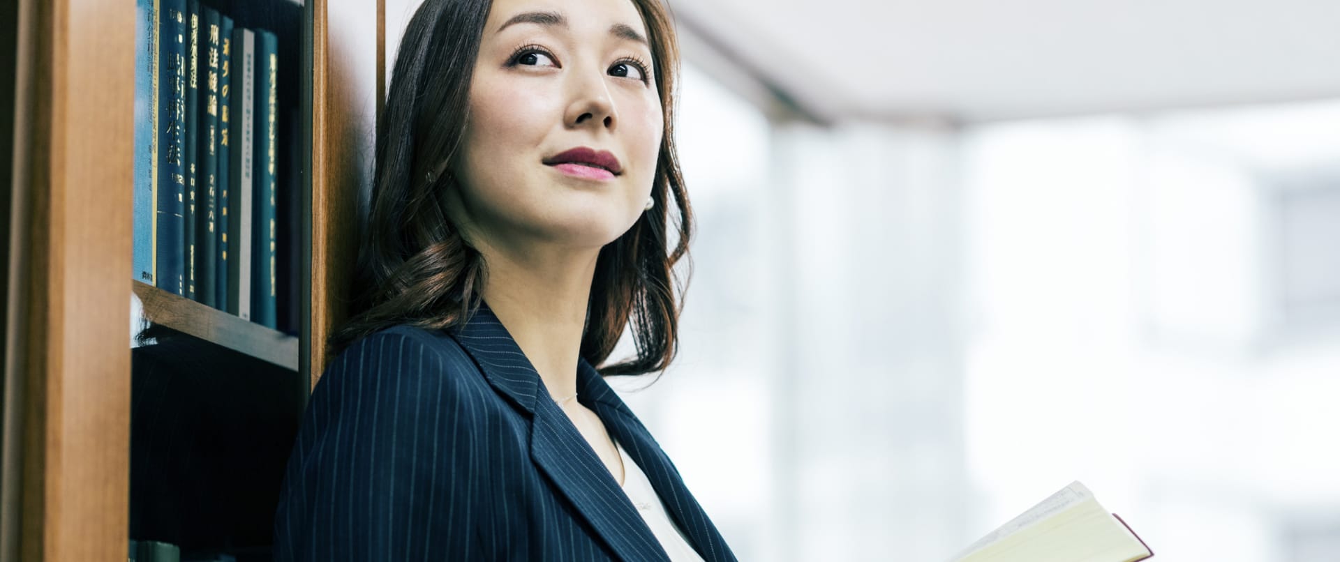本棚によりかかるビジネスウーマンの写真